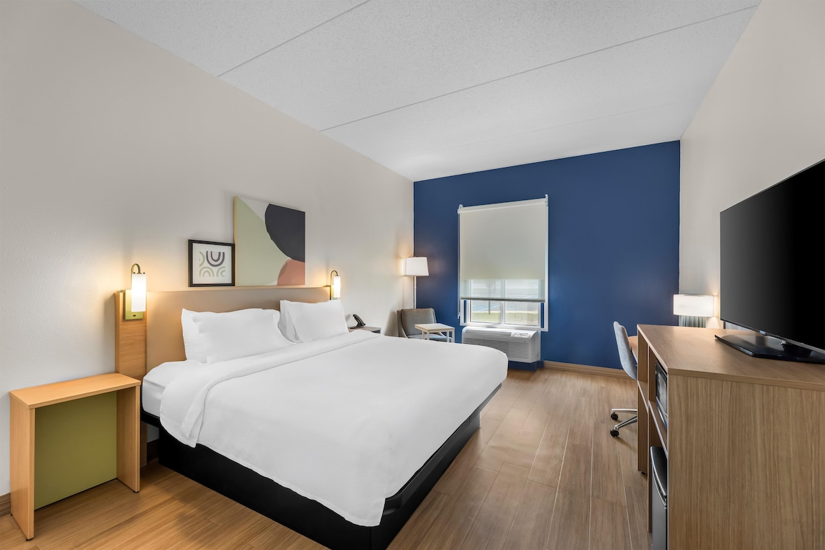 A hotel room with a bed, desk, TV, and a window.