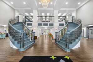 A spacious interior with a central staircase, a chandelier, and a view to the outdoors.