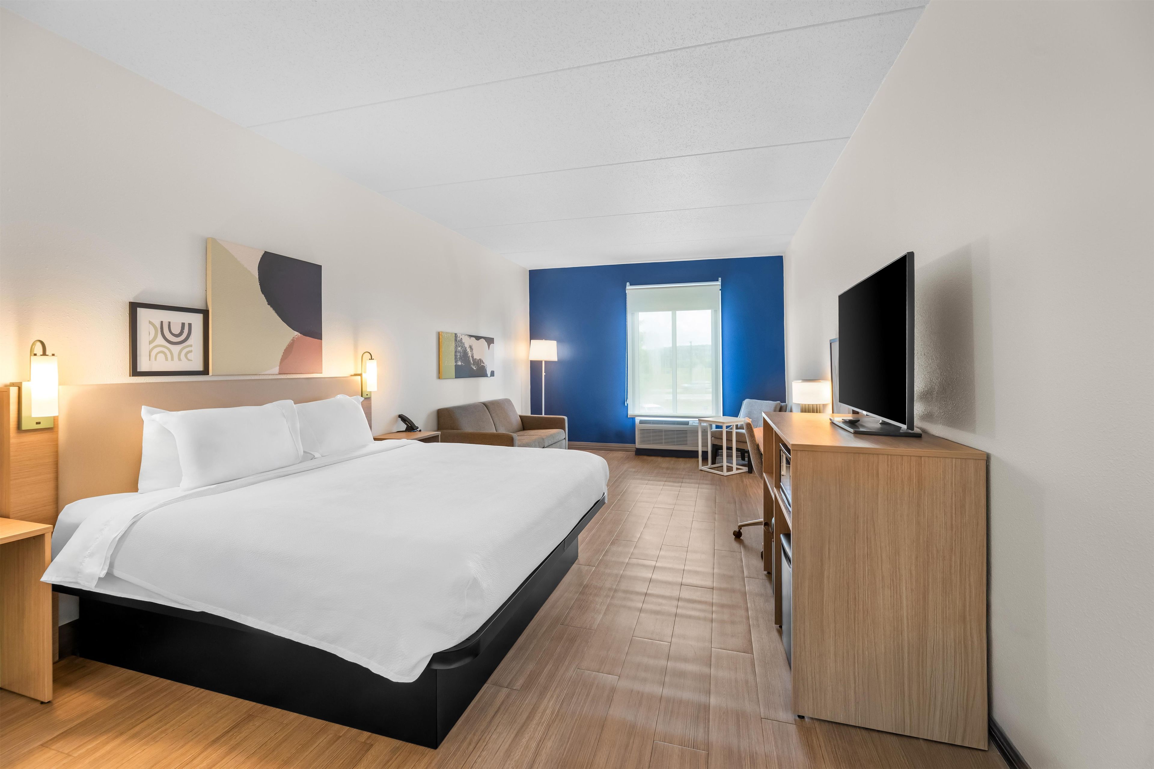 A hotel room with a bed, bedside tables, a desk, a chair, a TV, and artwork on the walls.
