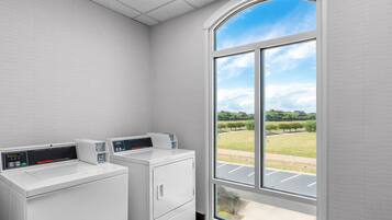 Een wasserette met twee witte wasmachines en drogers, een groot raam met uitzicht op een groen landschap.