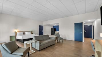 A hotel room with a bed, sofa, armchair, small table, and a desk.