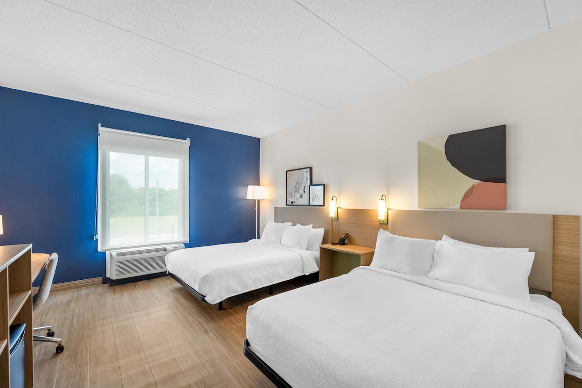 Habitación de hotel con dos camas, un escritorio, una silla, un ventanal y luces fijadas a la pared.