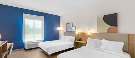 A hotel room with two beds, a desk, a chair, a window, and wall-mounted lights.