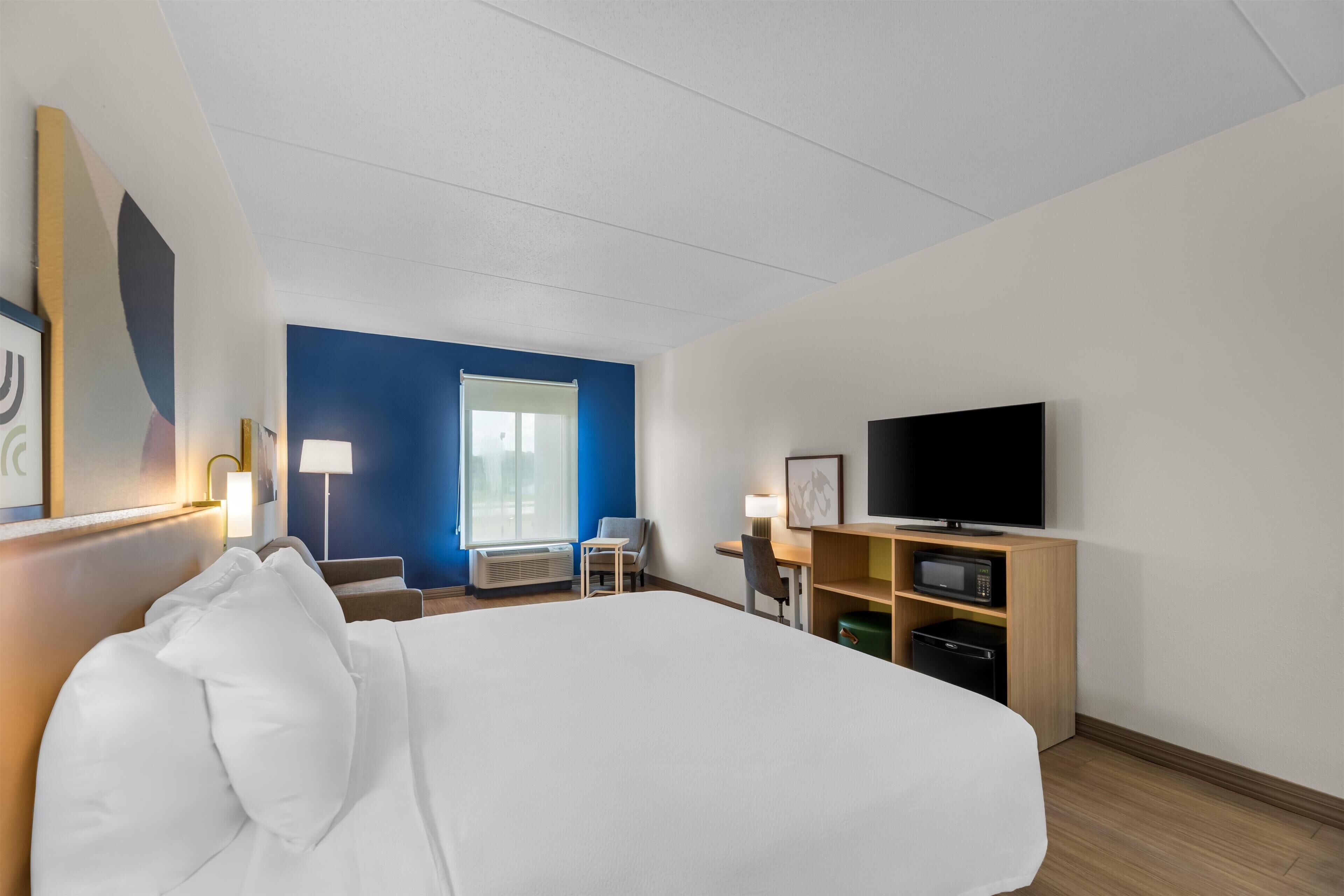 A hotel room with a large bed, a desk with a chair, a television, and a microwave.
