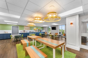 A modern dining area with wooden tables and benches, green chairs, and pendant lighting. - Spark by Hilton Tuscumbia Muscle Shoals (Tuscumbia)