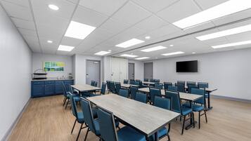 Una sala de conferencias con mesas, sillas, una kitchenette y un televisor de pantalla plana en la pared.