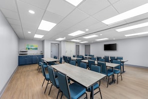 A conference room with tables and chairs, a kitchenette, and a flat-screen TV on the wall. - Spark by Hilton Tuscumbia Muscle Shoals (Tuscumbia)