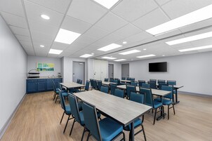 Una sala de conferencias con mesas, sillas, una kitchenette y un televisor de pantalla plana en la pared.