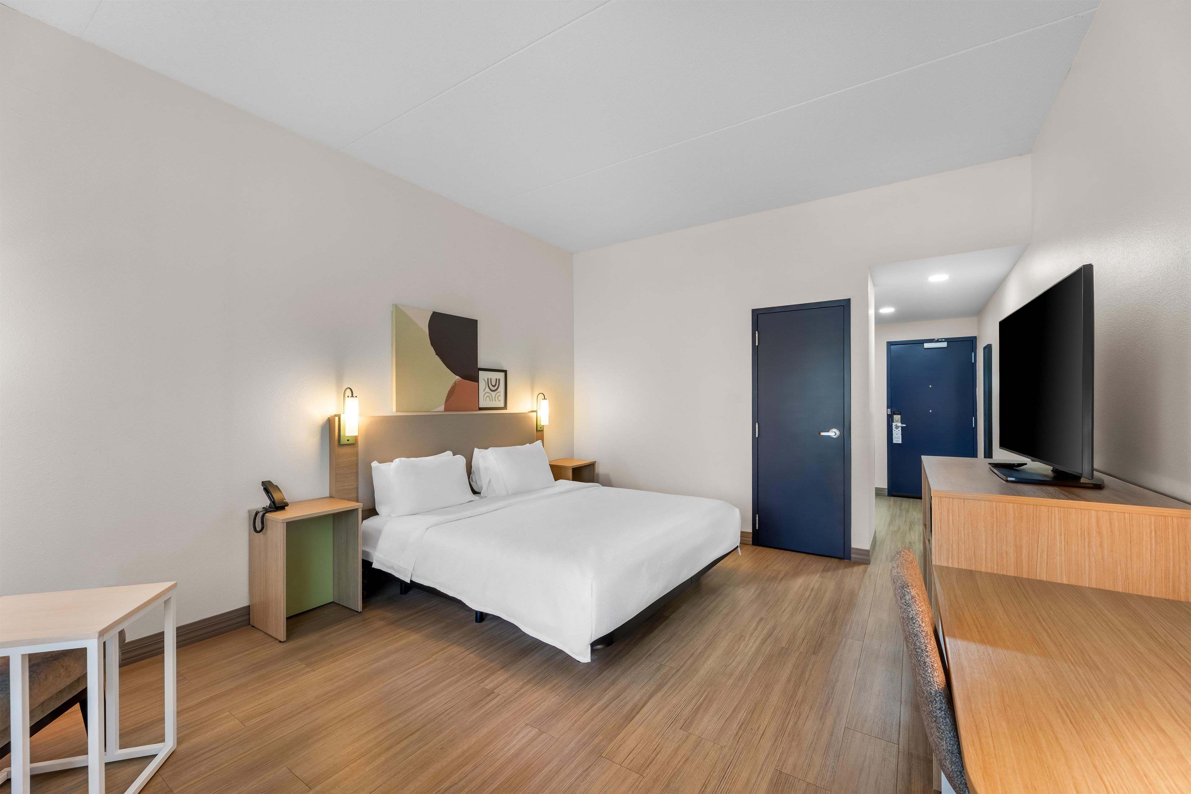 Et moderne hotelværelse med seng, sengebord, fjernsyn og skrivebord.