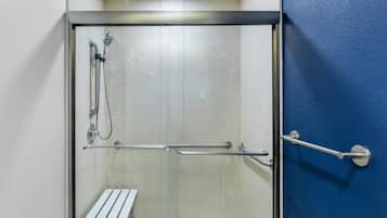 A glass-enclosed shower area with a bench, a handrail, and a door with a blue wall.