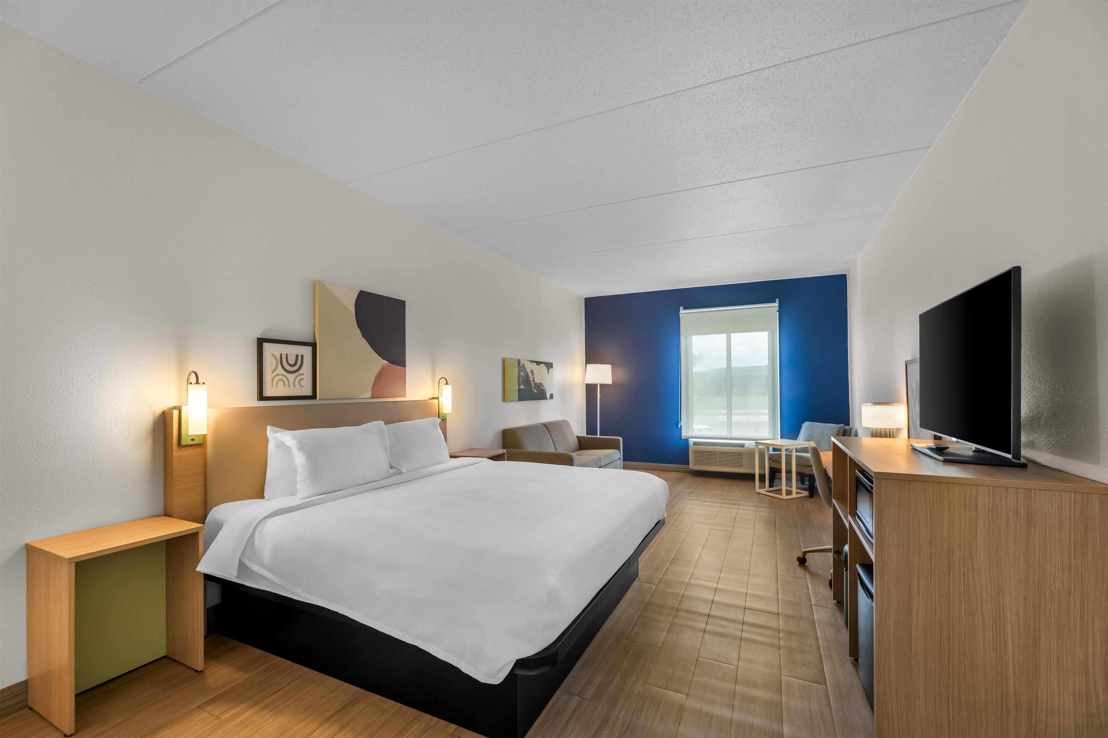 Una habitación de hotel con cama, mesitas de noche, escritorio, televisión y obras de arte en las paredes.