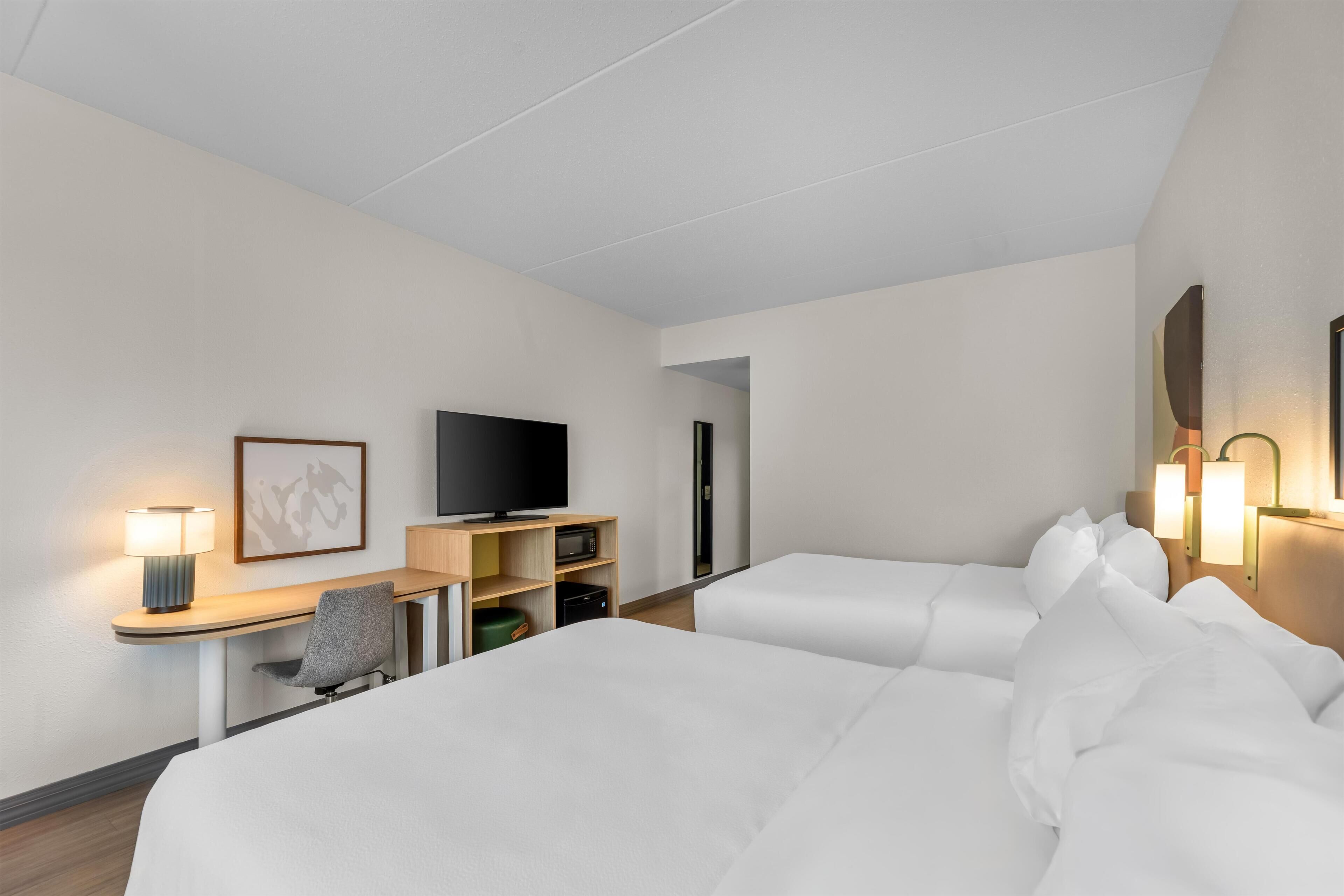 A hotel room with two beds, a desk with a TV, a lamp, and a chair.