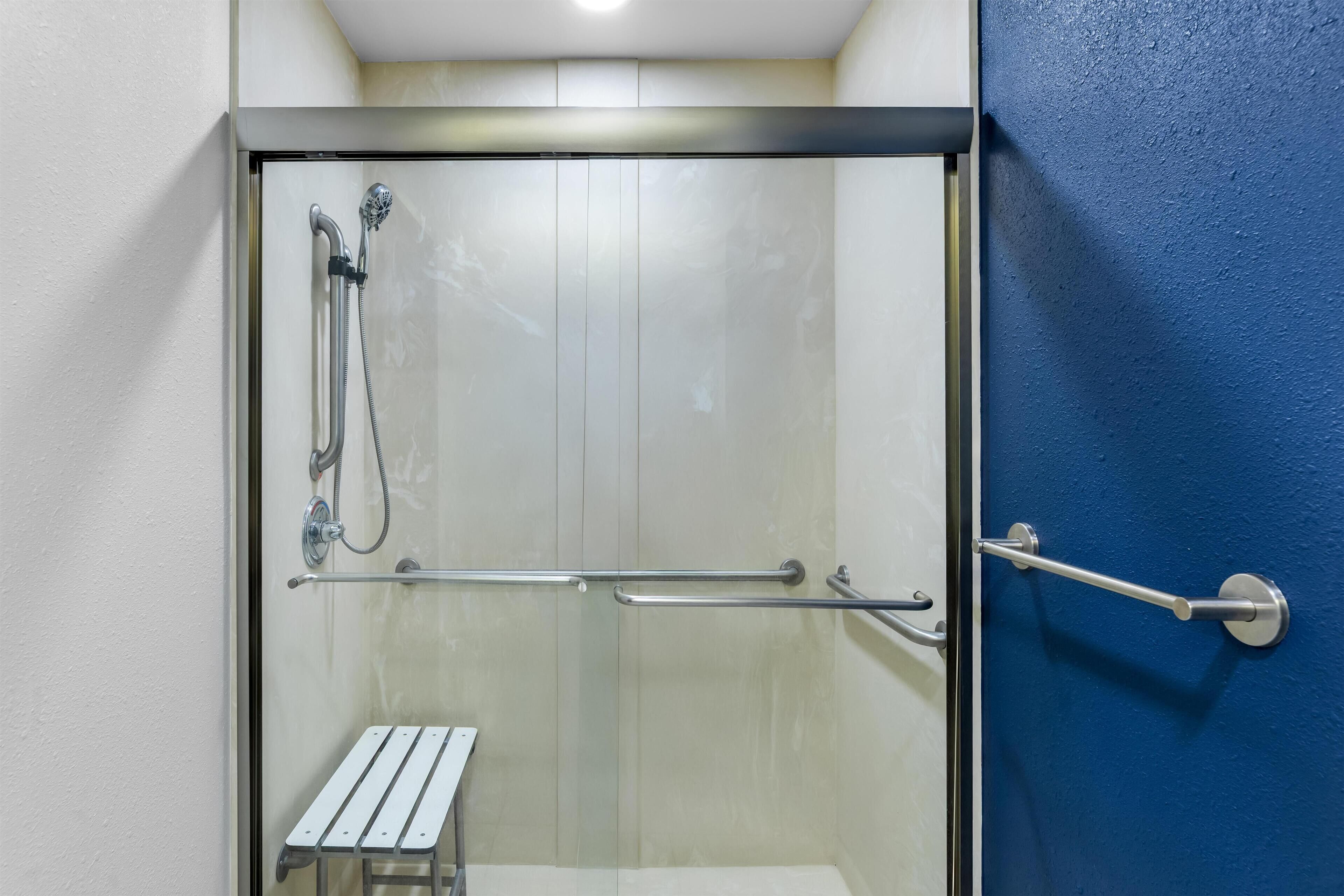 A glass-enclosed shower area with a bench, a handrail, and a door with a blue wall.