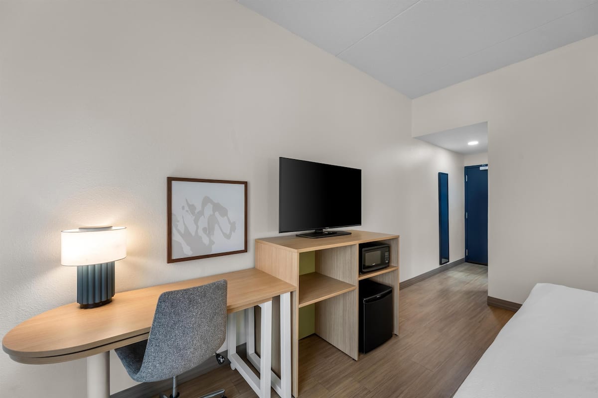 Una habitación de hotel con escritorio, silla, televisor, microondas y refrigerador.