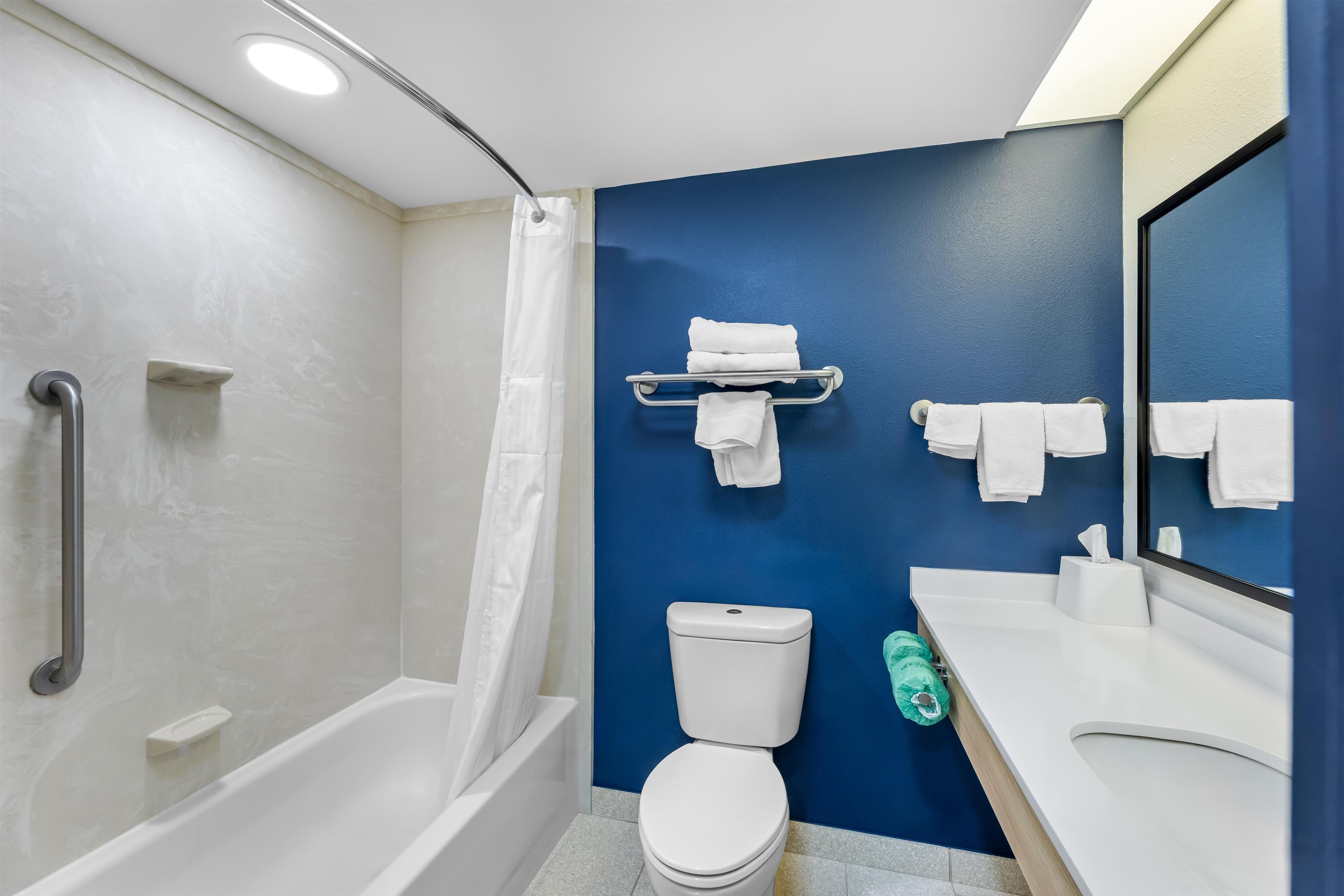 Un baño moderno con bañera, inodoro y lavamanos, que presenta una pared azul de acento y un espejo.
