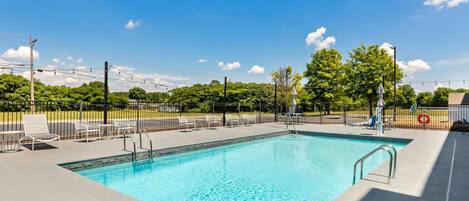 A rectangular swimming pool with a tiled edge, surrounded by a concrete deck, metal railings, and white lounge chairs.