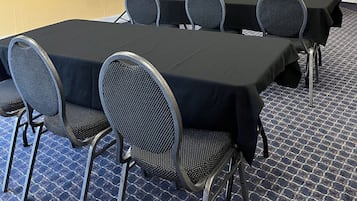 A conference room with a long table, chairs, a projector screen, and a small cabinet.