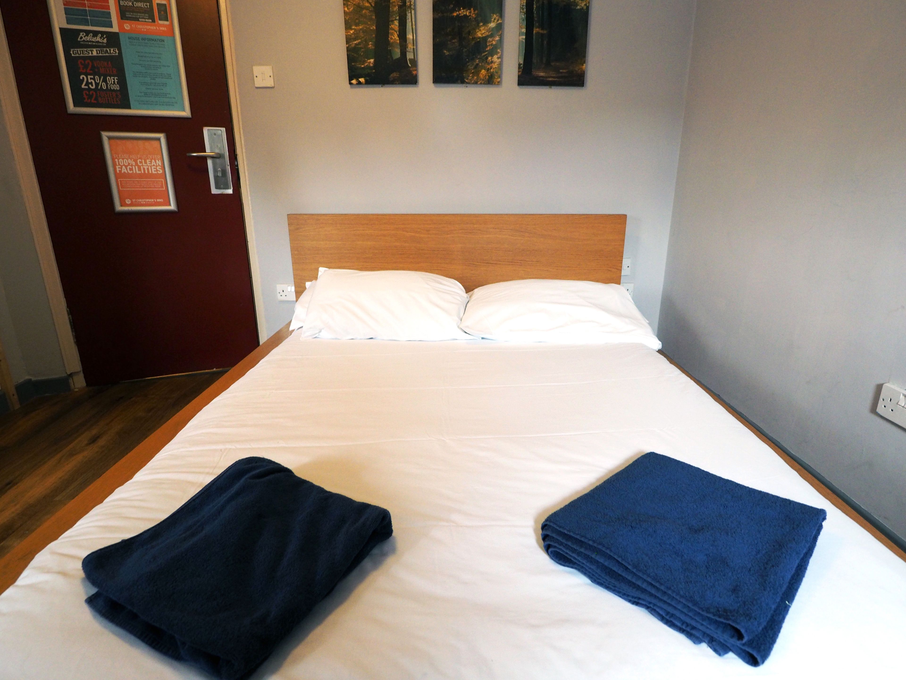 A neatly made bed with white linens, a wooden headboard, and two folded towels.