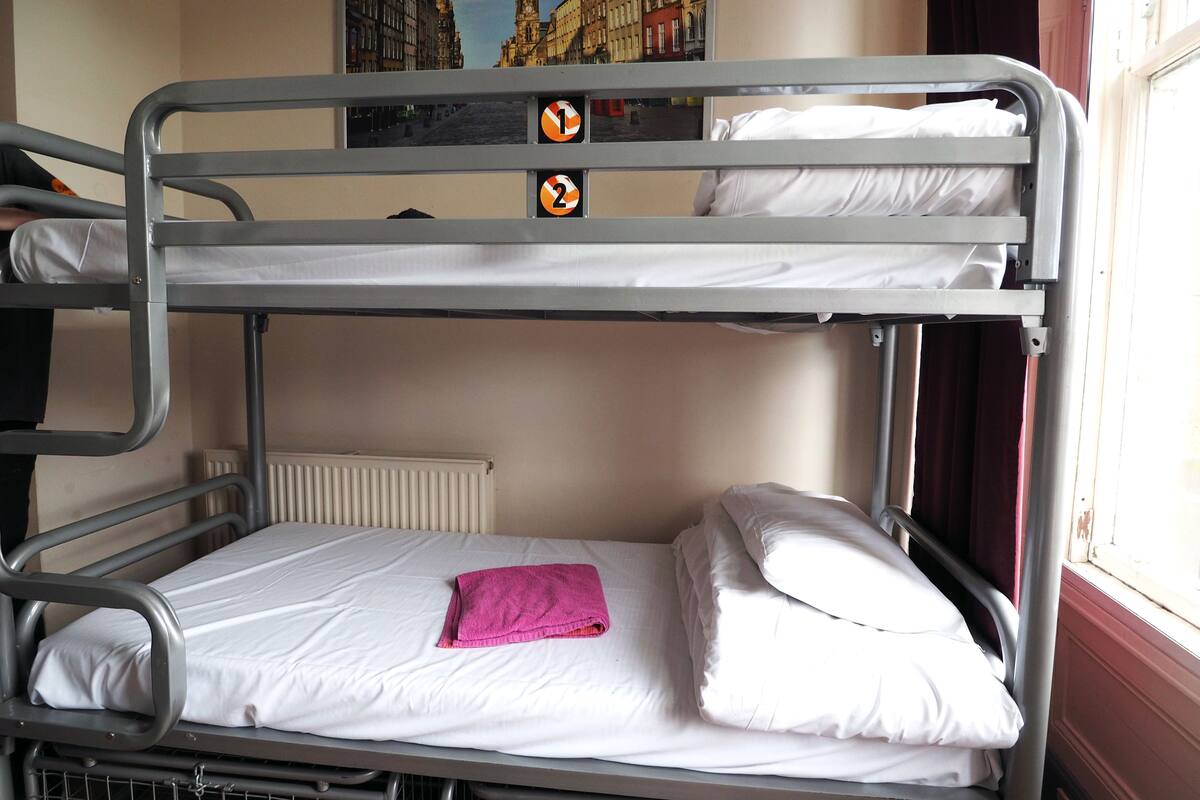 A bunk bed with two levels, white bedding, and a pink towel on the lower bunk.
