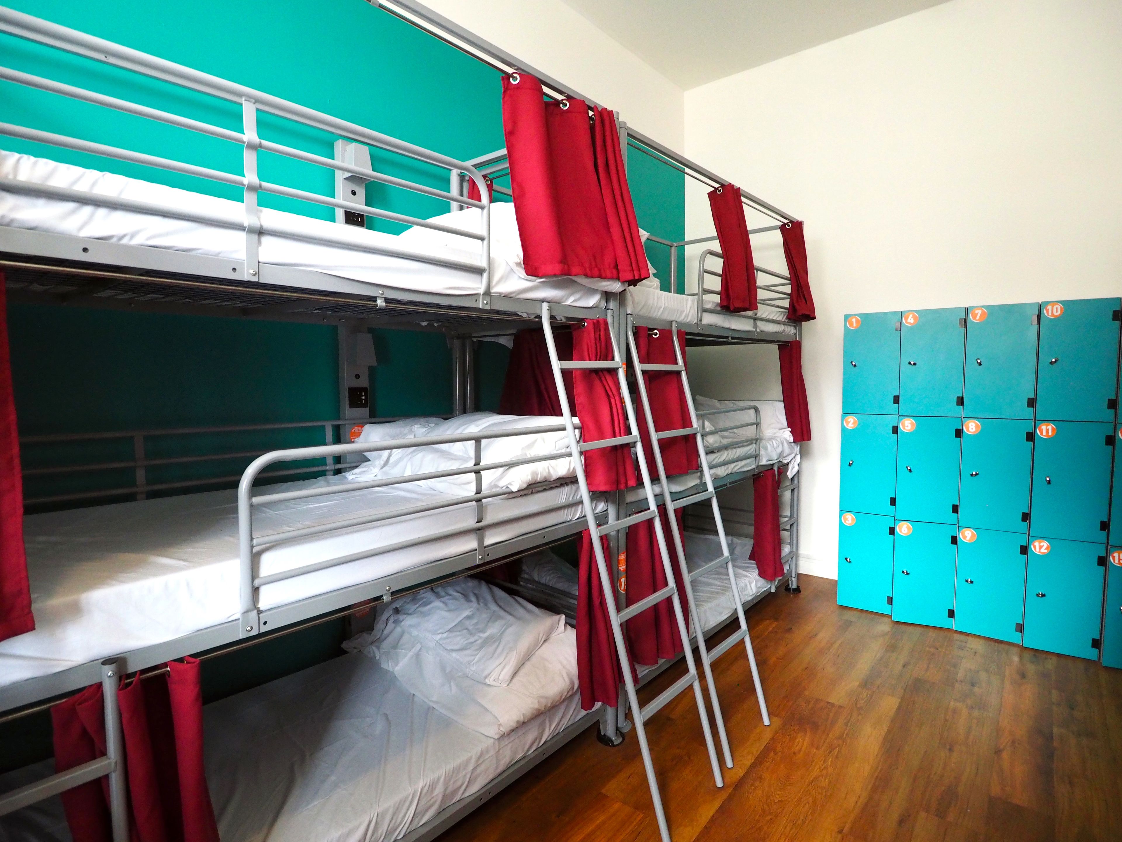 Camera con letto a castello, una scala, tende rosse e una fila di armadietti.