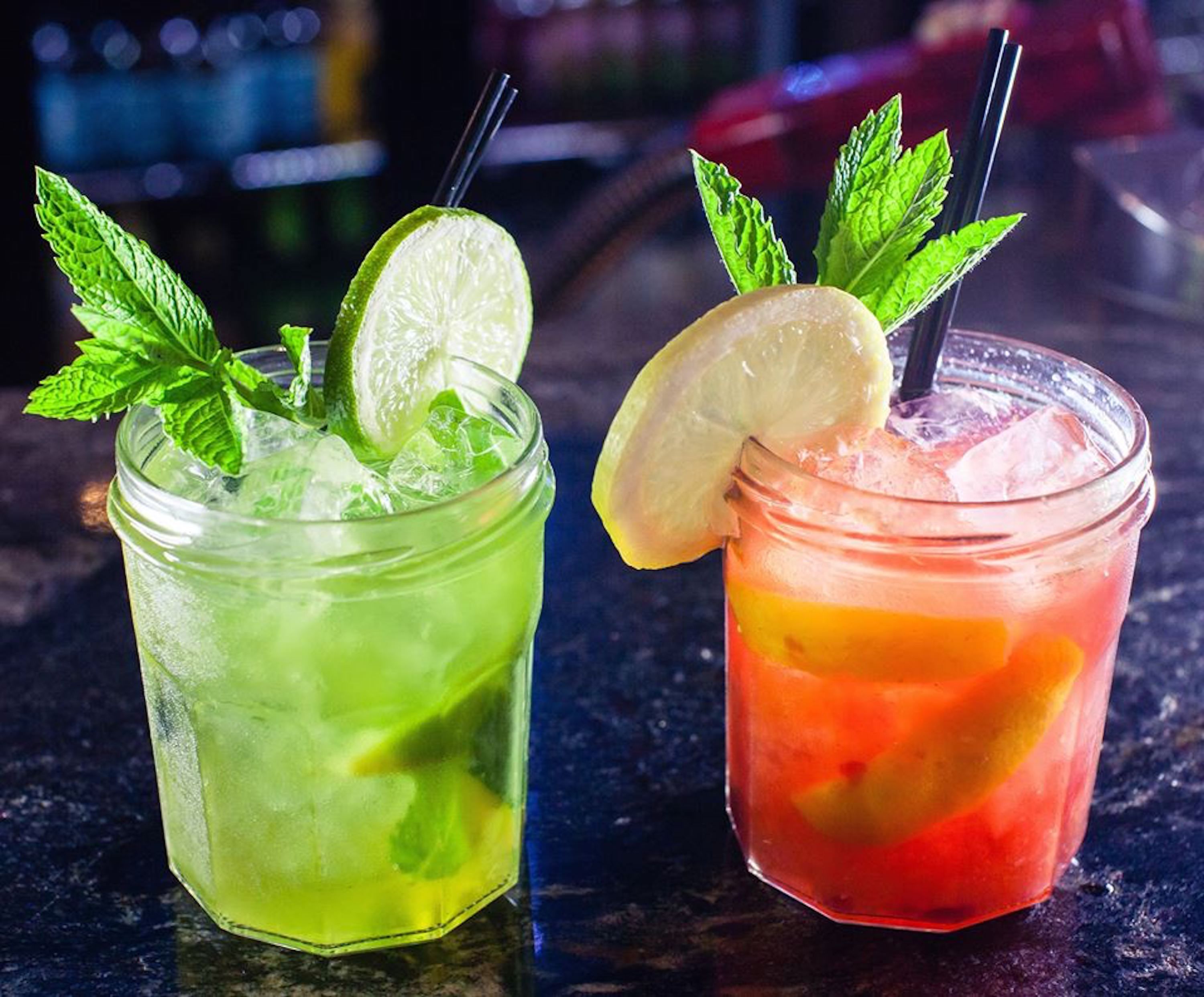 Two drinks in glasses with straws and lime slices, garnished with mint leaves.