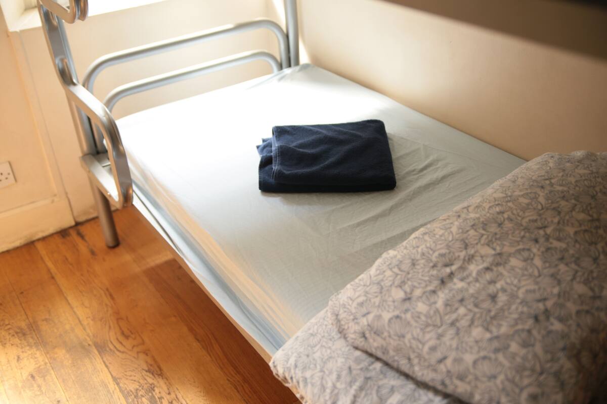 A single bed with a folded dark blue towel, a metal headboard, and a wooden floor.