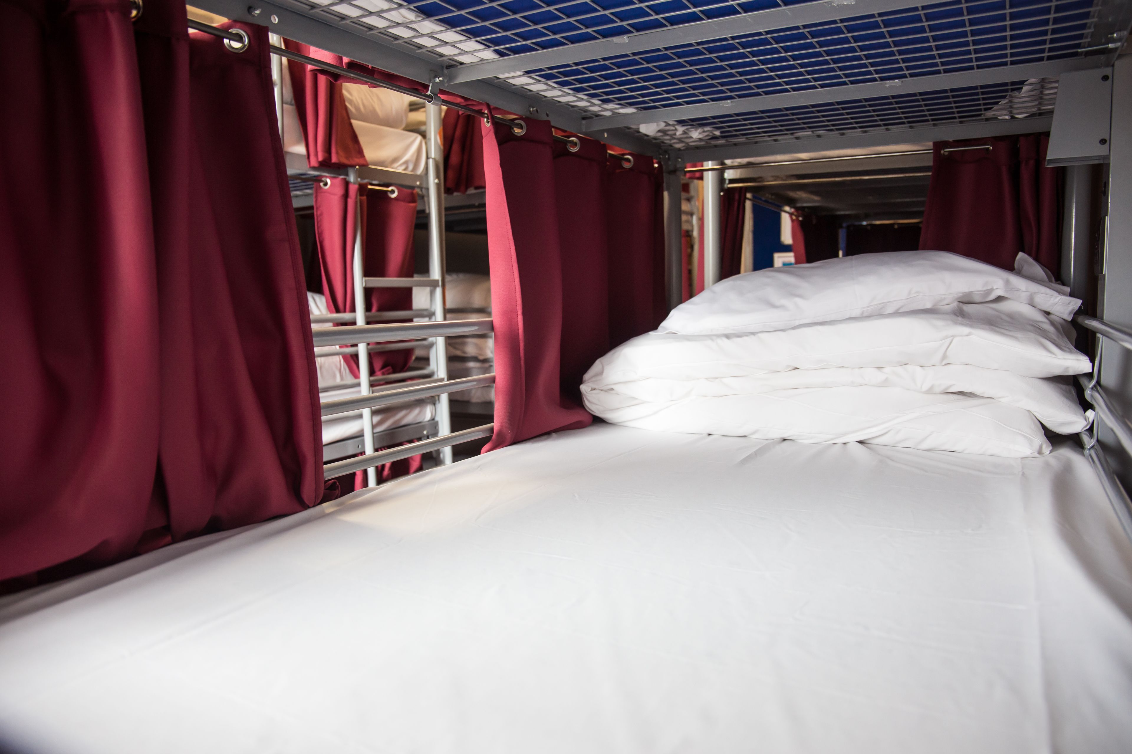Una cama litera con cortinas rojas, ropa de cama blanca y una escalera de metal.