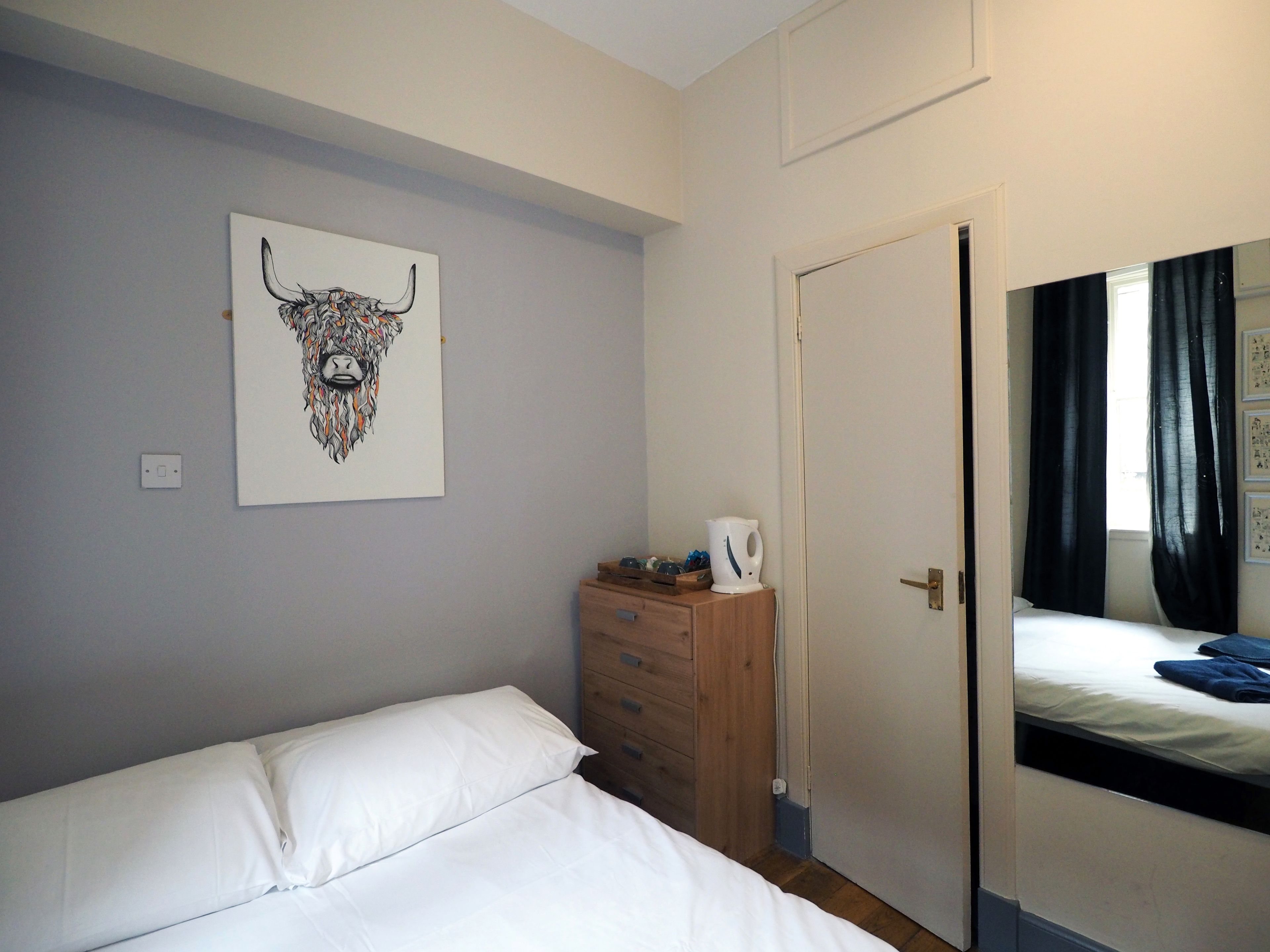 A bedroom with a bed, a dresser, a door, and a wall-mounted artwork.