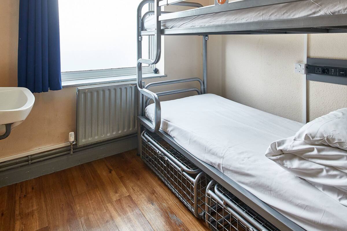 A bunk bed room with a window, a radiator, and a sink.
