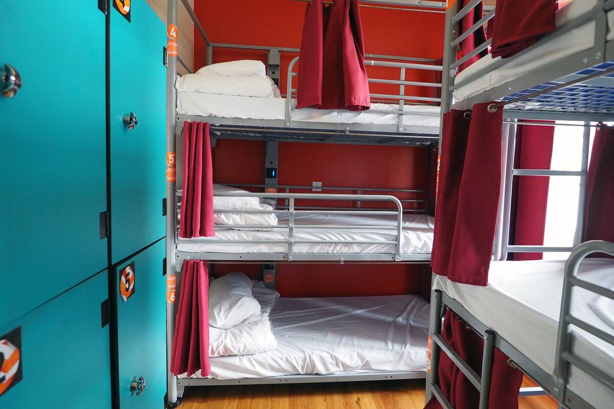 A bunk bed room with red curtains, a teal-colored wardrobe, and a wooden floor.