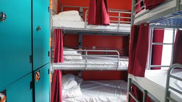 A bunk bed room with red curtains, a teal-colored wardrobe, and a wooden floor.