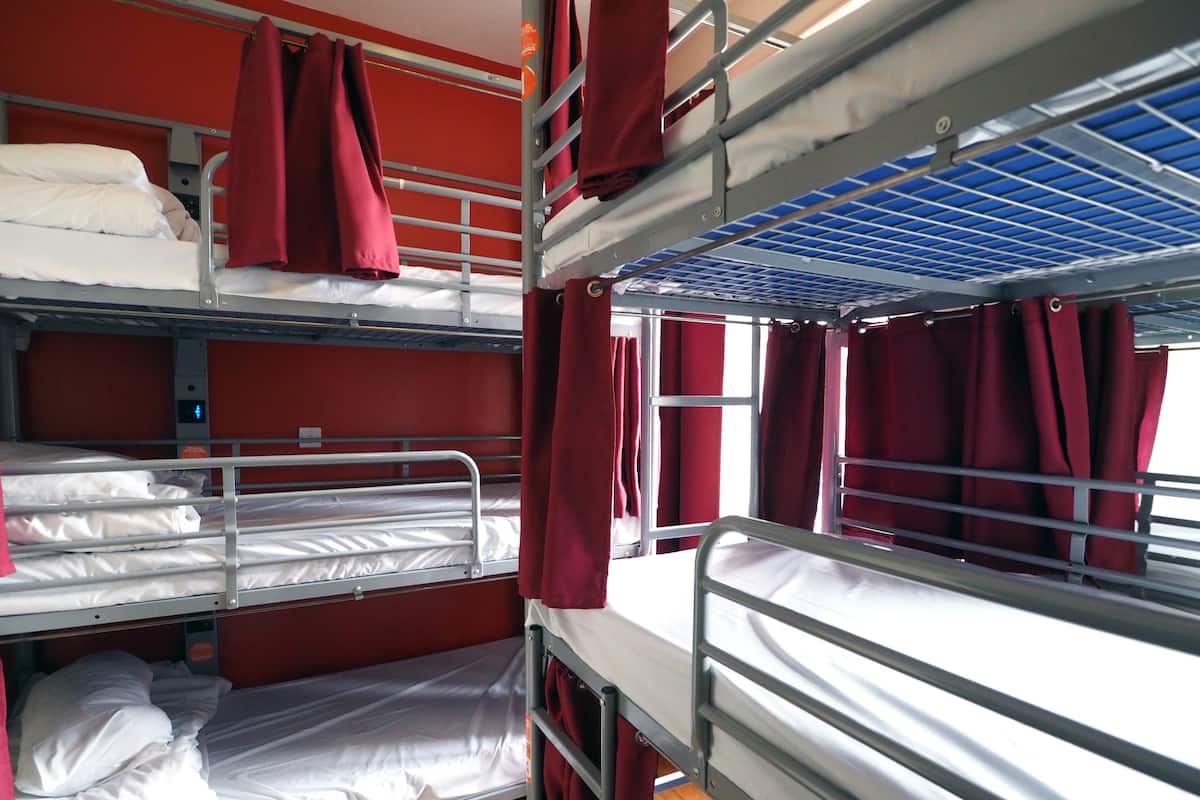 A bunk bed room with red curtains, a digital clock, and a window with curtains.