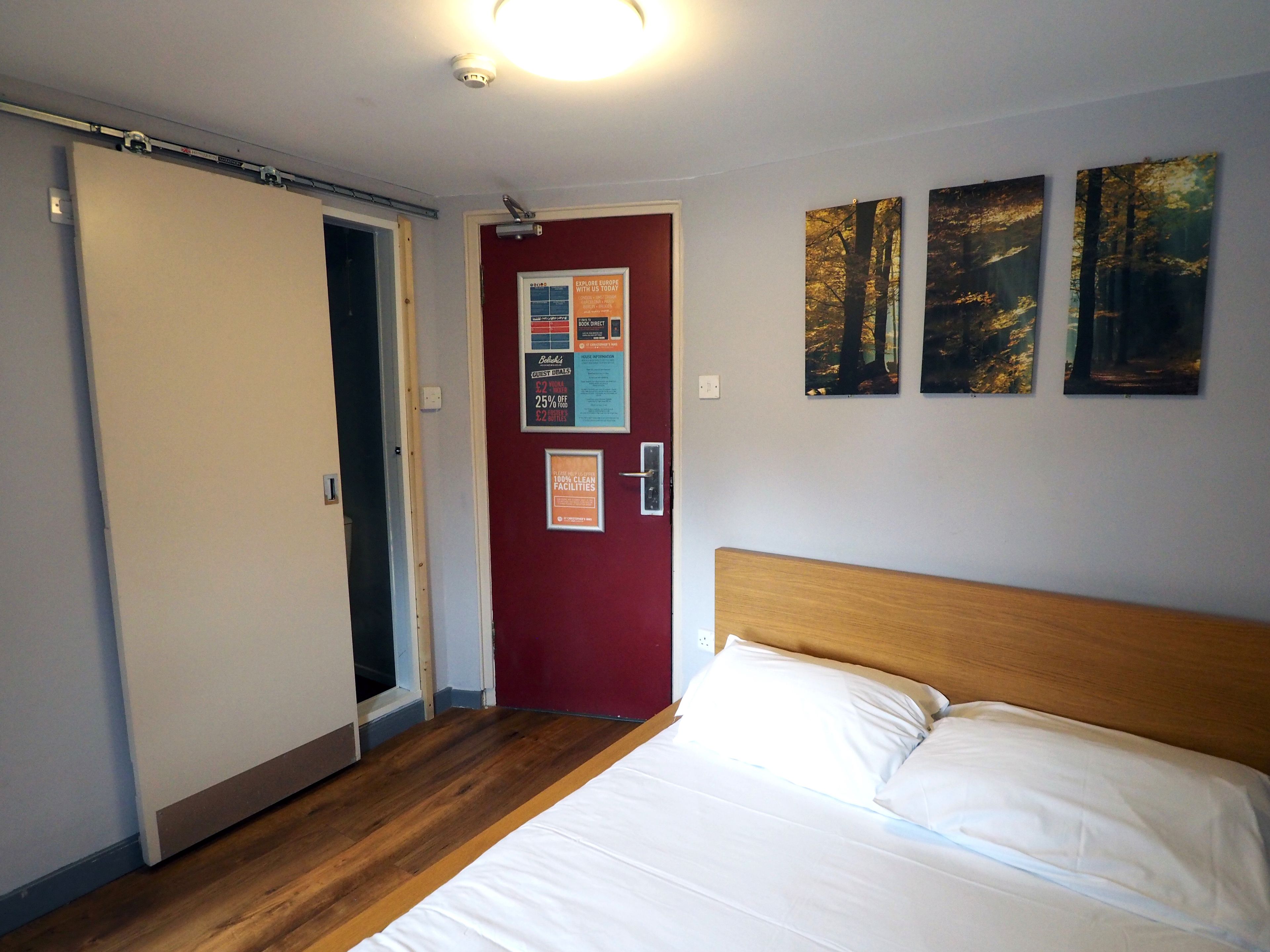 Une chambre d’hôtel avec un lit, une porte rouge et une affiche accrochée au mur.