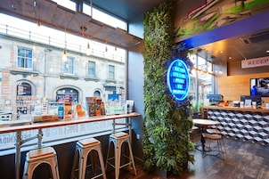 A bar area with a neon sign, bar stools, and a reception desk.