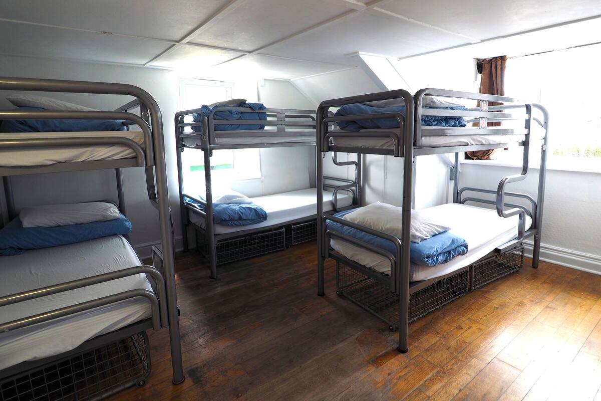 A room with bunk beds arranged in a row, wooden flooring, and a window with curtains.