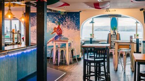 A restaurant with a bar area, stools, and a view of the sea through a large window. - St Christopher's Inn, Newquay - Hostel (Newquay)