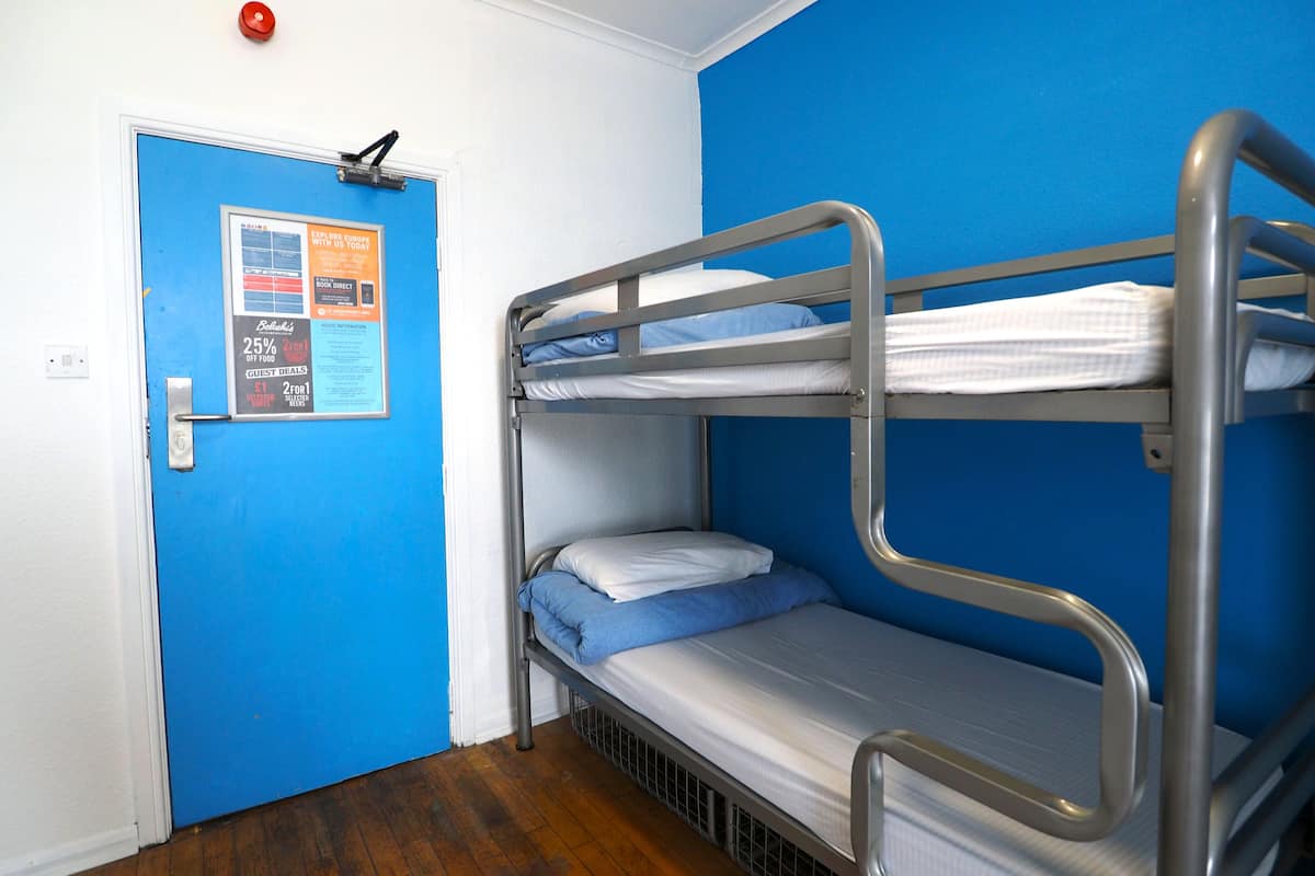 A bunk bed room with a blue wall, a door with a poster, and a red emergency button.