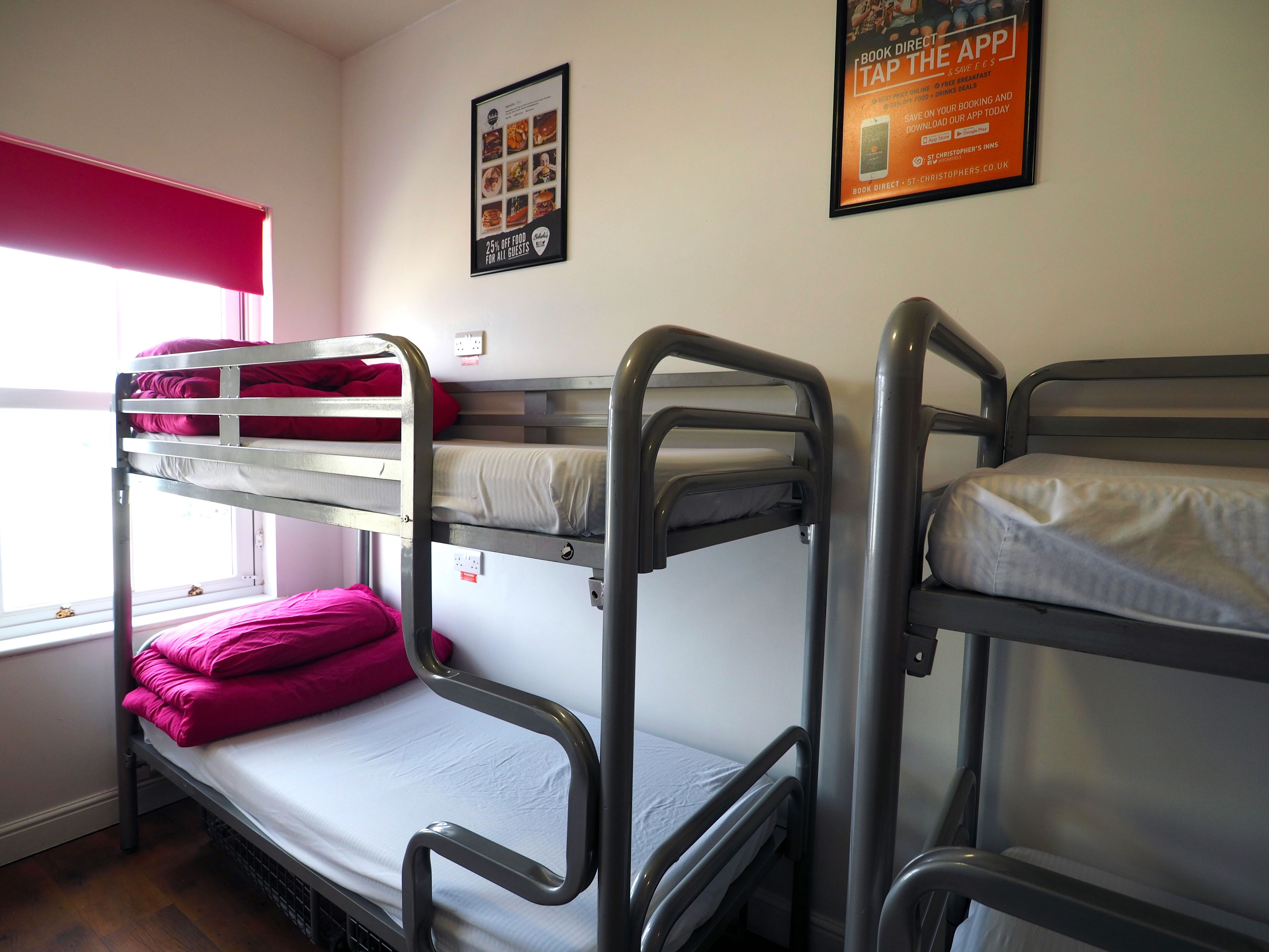 Ein Zimmer mit Etagenbetten, einem Poster an der Wand und einem Fenster mit rotem Rollo.