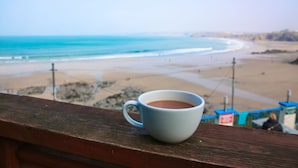 A white cup on a wooden ledge overlooking a beach with clear skies. - St Christopher's Inn, Newquay - Hostel (Newquay)