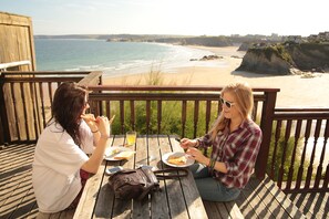 Two people dining at an outdoor wooden table with a view of the beach and cliffs. - St Christopher's Inn, Newquay - Hostel (Newquay)