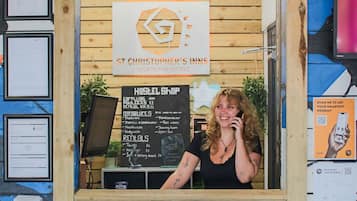 A reception area with a wooden facade, a sign reading "RECEPTION," and a menu board for "ST CHRISTOPHER'S INNS BACKPACKER HOSTELS" listing amenities like "BEDROOMS," "MINDFULNESS," and "RENTALS."