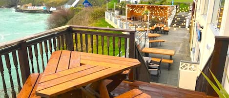En træterrasse med picnicborde med udsigt over en kystby.
