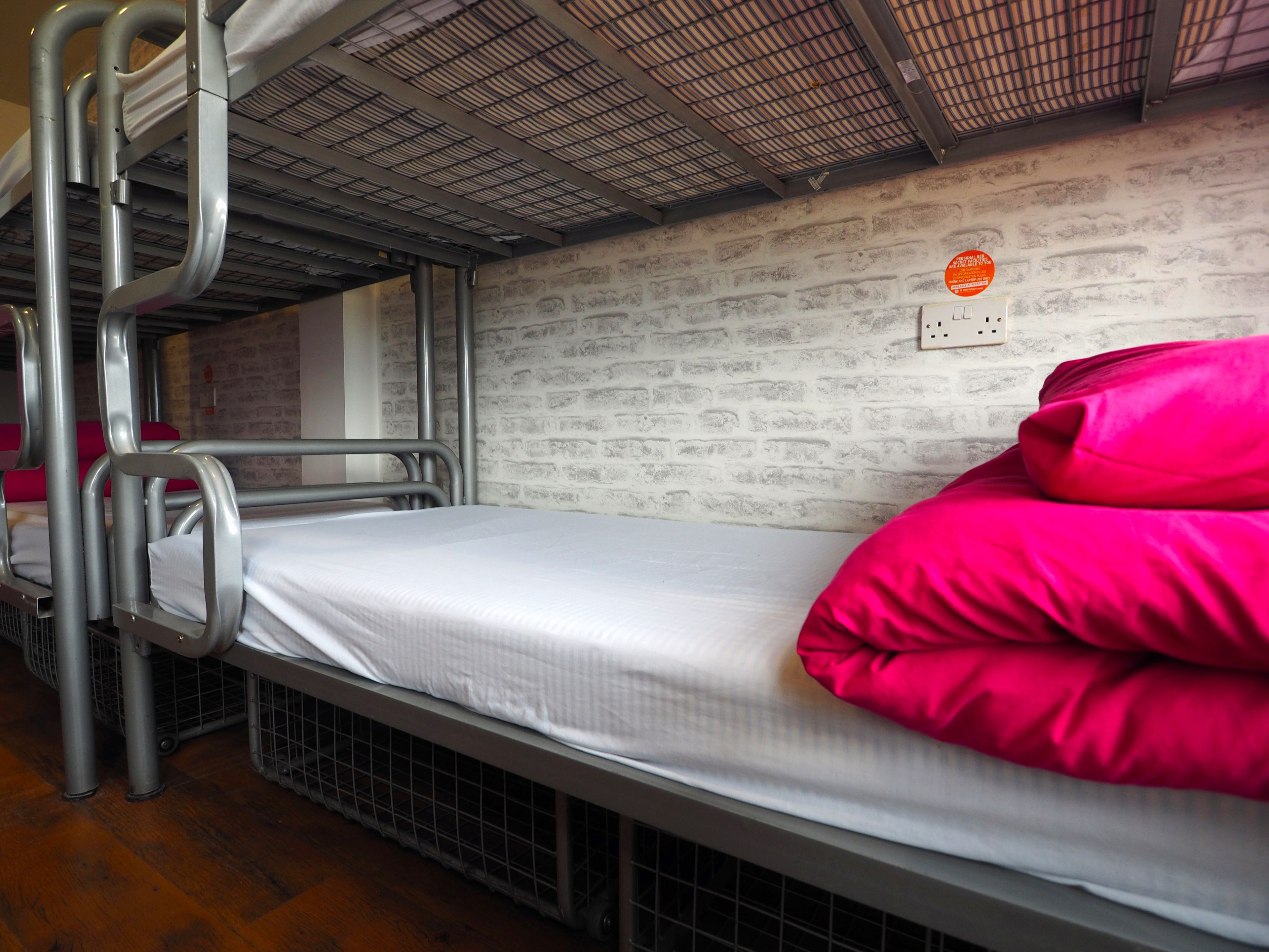 Een stapelbed met metalen spijlen en een bakstenen muur.