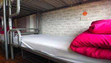 Een stapelbed met metalen spijlen en een bakstenen muur.