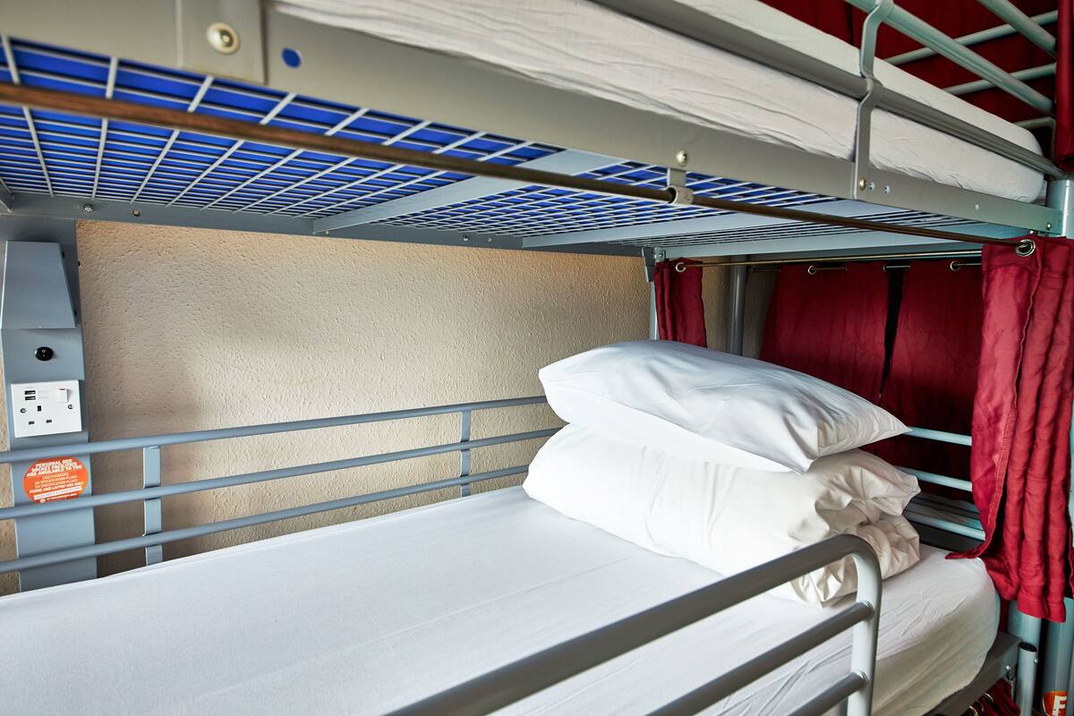 A bunk bed with a mattress and pillows, a metal headboard, and a red curtain.