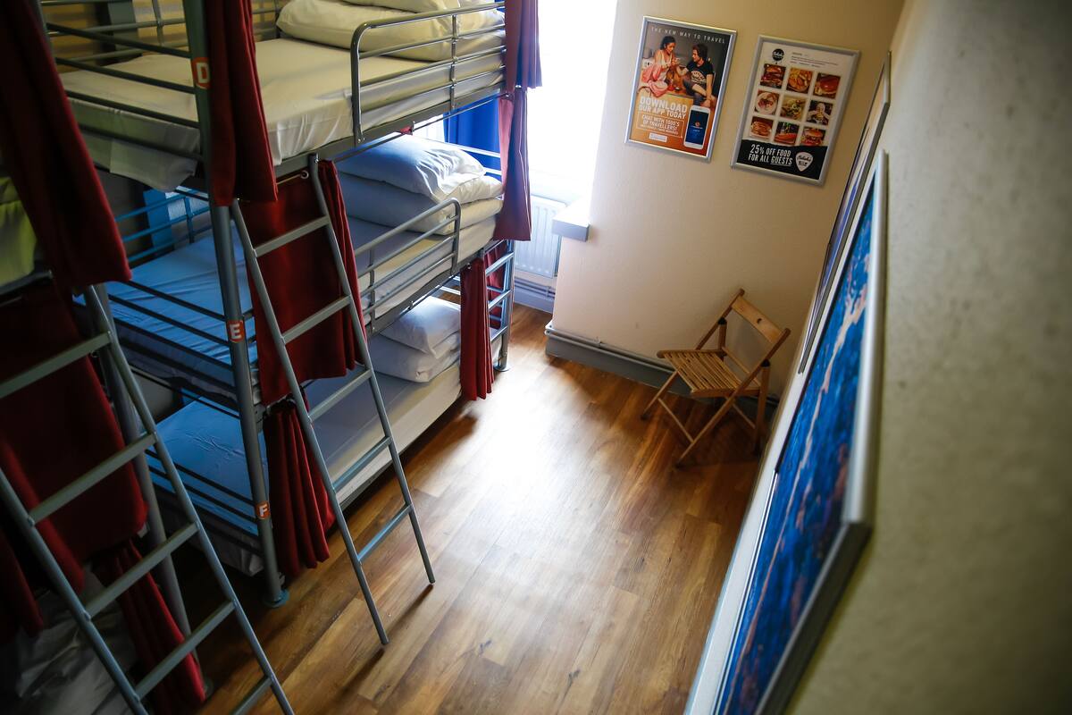 A dormitory room with bunk beds, a wooden floor, and a small wooden chair.