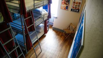 Une chambre de dortoir avec des lits superposés, un plancher en bois et une petite chaise en bois.