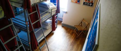 A dormitory room with bunk beds, a wooden floor, and a small wooden chair.