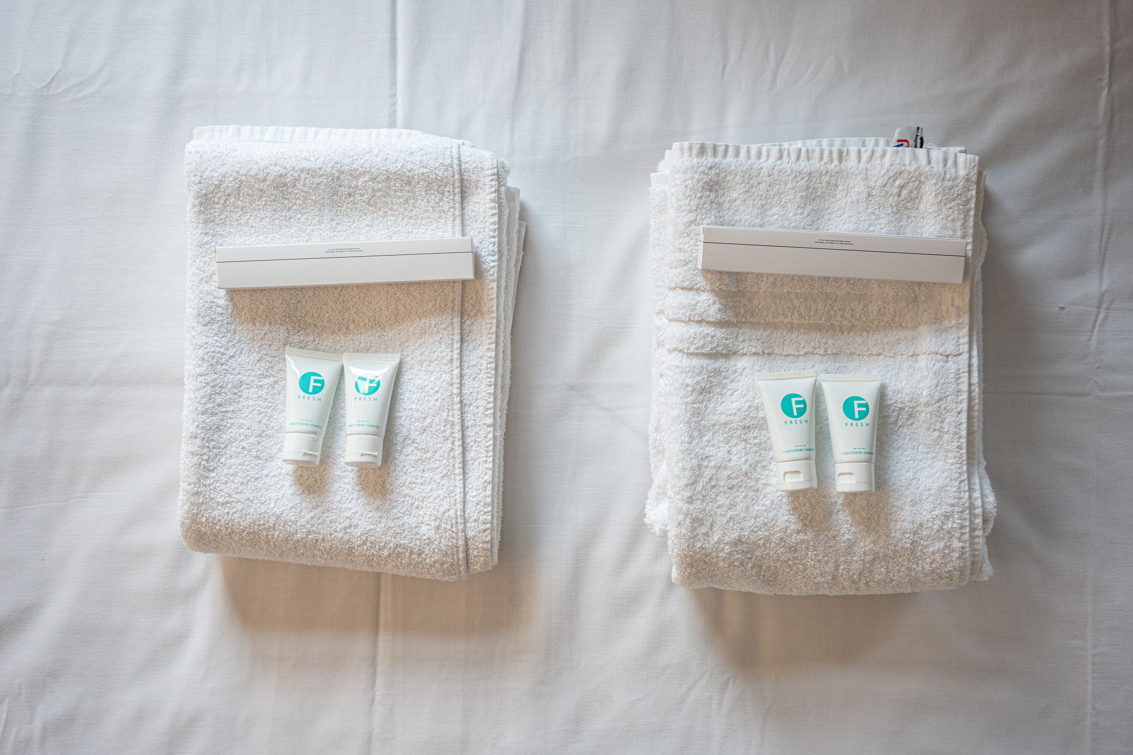 Two neatly folded white towels with a white towel rack and two tubes of lotion on a white bedspread.