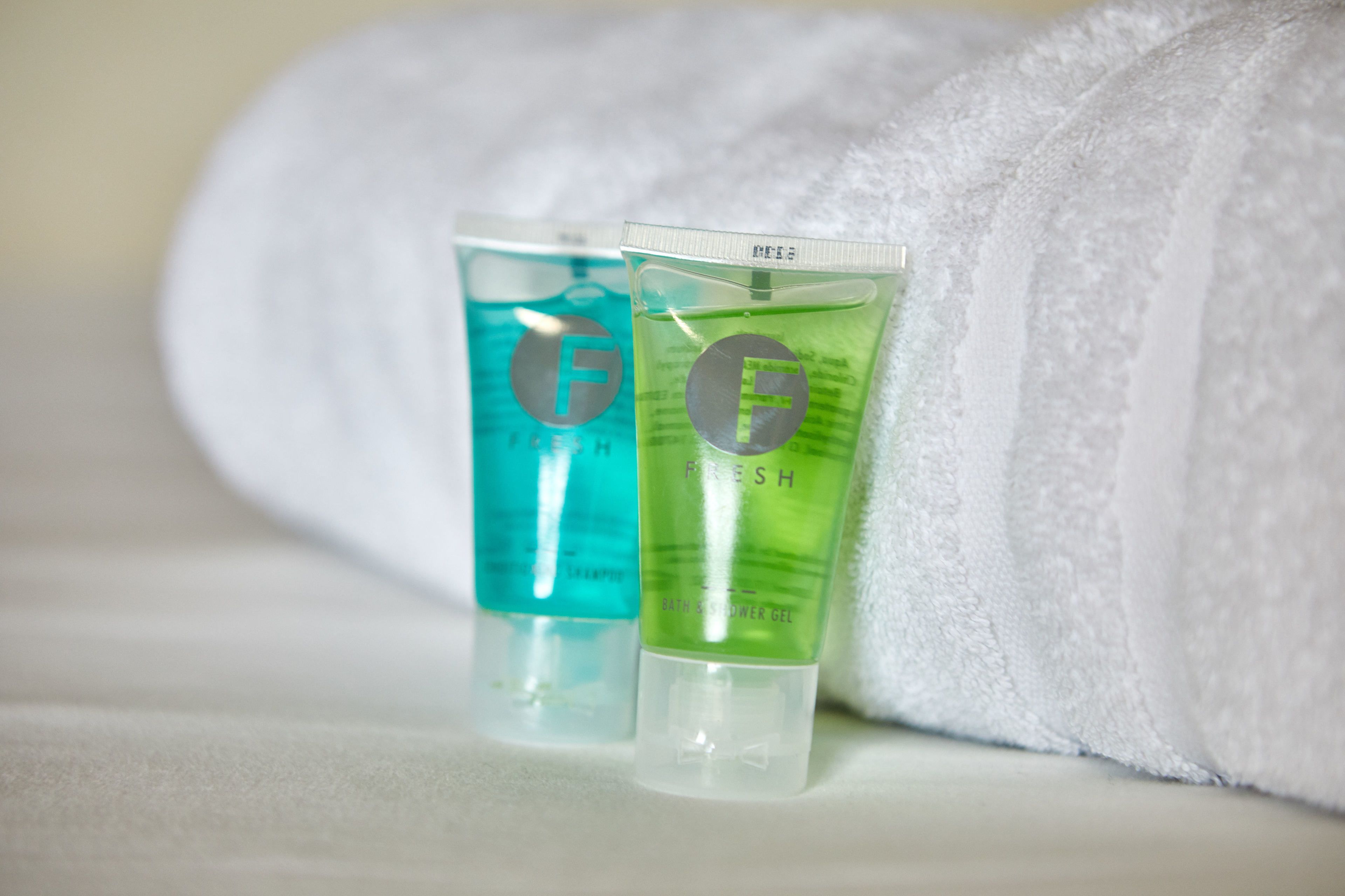 Two tubes of bath and shower gel on a white surface with a white towel in the background.